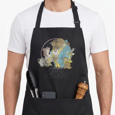 Shot sleeping beauty apron - Beast Belle Lumiere Cogsworth Mrs Potts circular frame cartoon art — shown on a black cotton canvas apron against a white background
