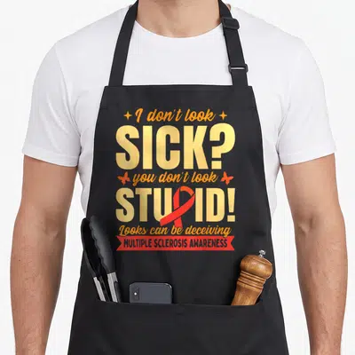 Cute multiple sclerosis awareness apron - Yellow and orange text reading I don't look SICK with red ribbon overlapping — shown on a black cotton canvas apron against a white background