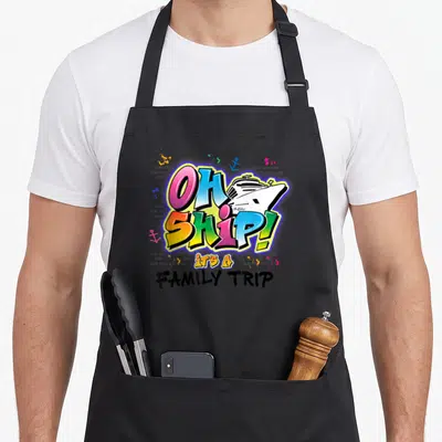 Ship vacation family aprons - Cartoon OH SHIP text with cruise ship, anchors, and splatters on grey brick — shown on a black cotton canvas apron against a white background
