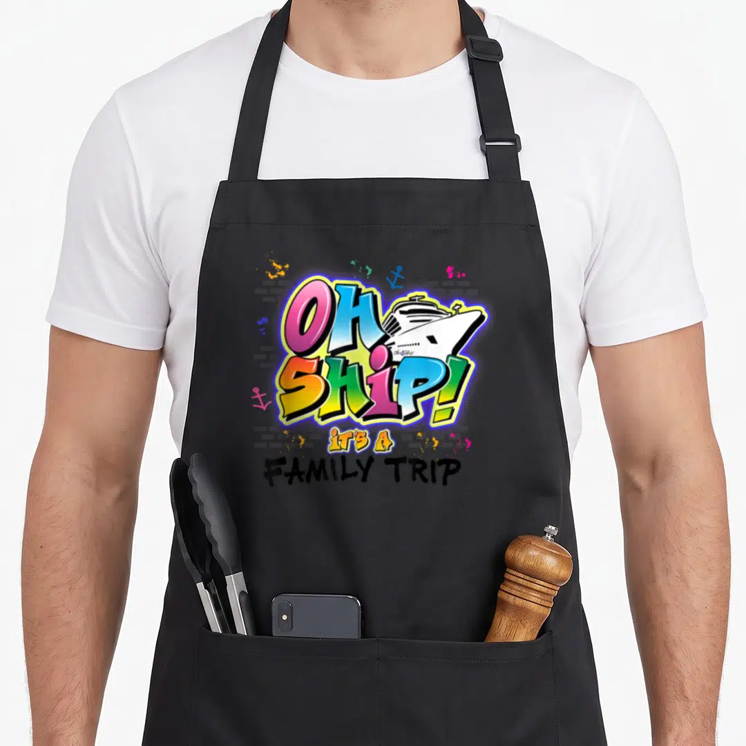 Ship vacation family aprons - Cartoon OH SHIP text with cruise ship, anchors, and splatters on grey brick — shown on a black cotton canvas apron against a white background