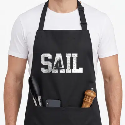 Sail sailing apron - White SAIL text with sailboat silhouette inside the A, distressed texture on black fabric — shown on a black cotton canvas apron against a white background