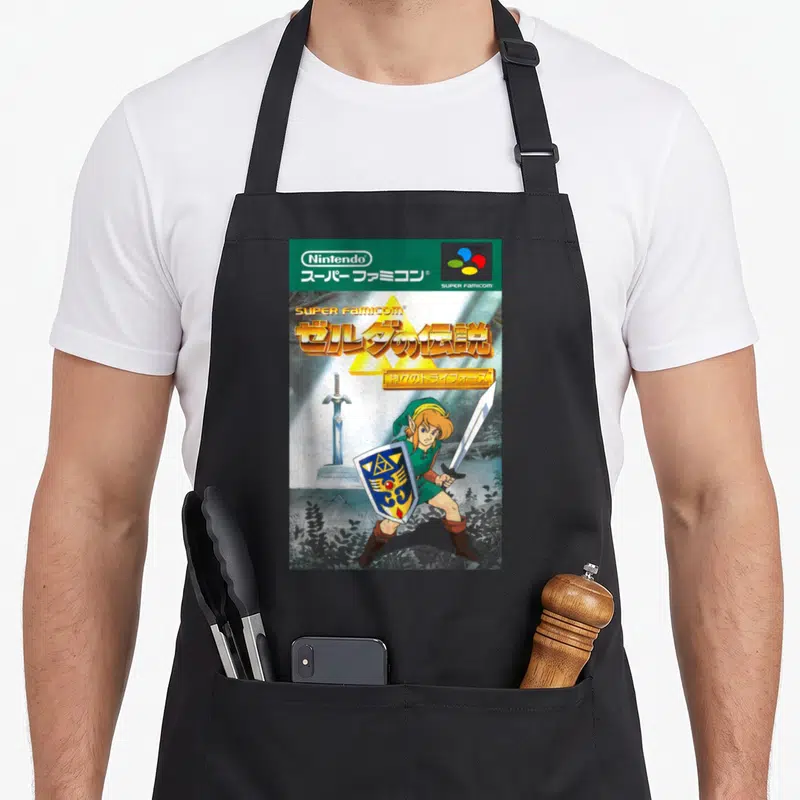 Japanese cover apron - Link holding sword and shield under Super Famicom and Japanese text logos — shown on a black cotton canvas apron against a white background