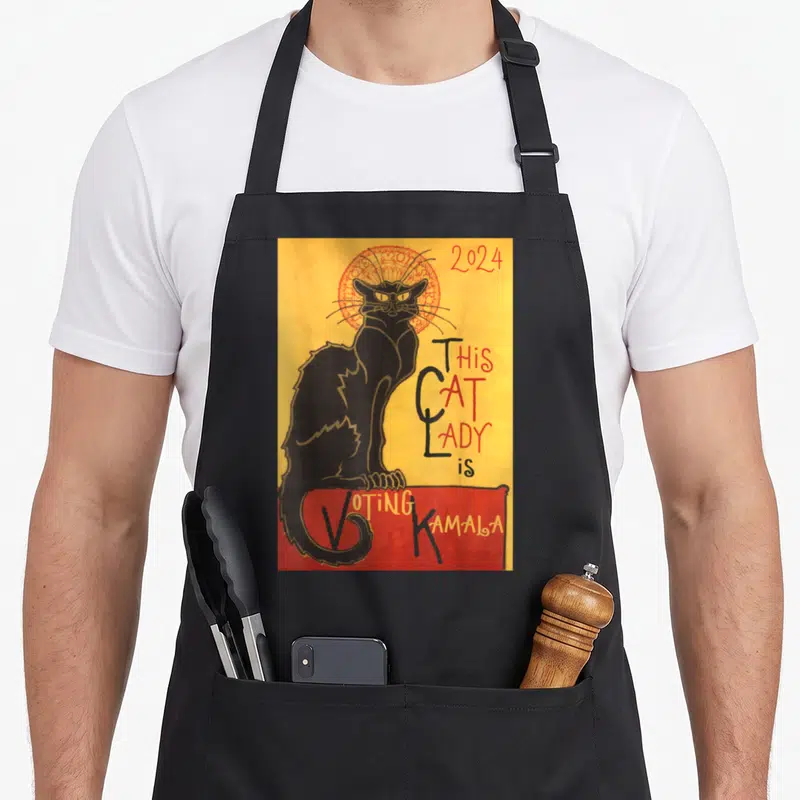 Chat cat lady apron - Black cat with red halo on yellow background holding red voting banner with 2024 text — shown on a black cotton canvas apron against a white background