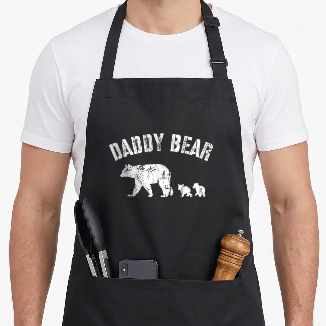 Cub daddy apron - Arched DADDY BEAR text above white bear and two cubs walking left — shown on a black cotton canvas apron against a white background
