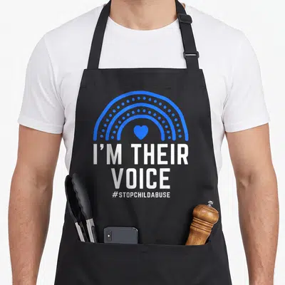Their child abuse prevention apron - Blue rainbow arch with heart and white I'M THEIR VOICE stacked text — shown on a black cotton canvas apron against a white background