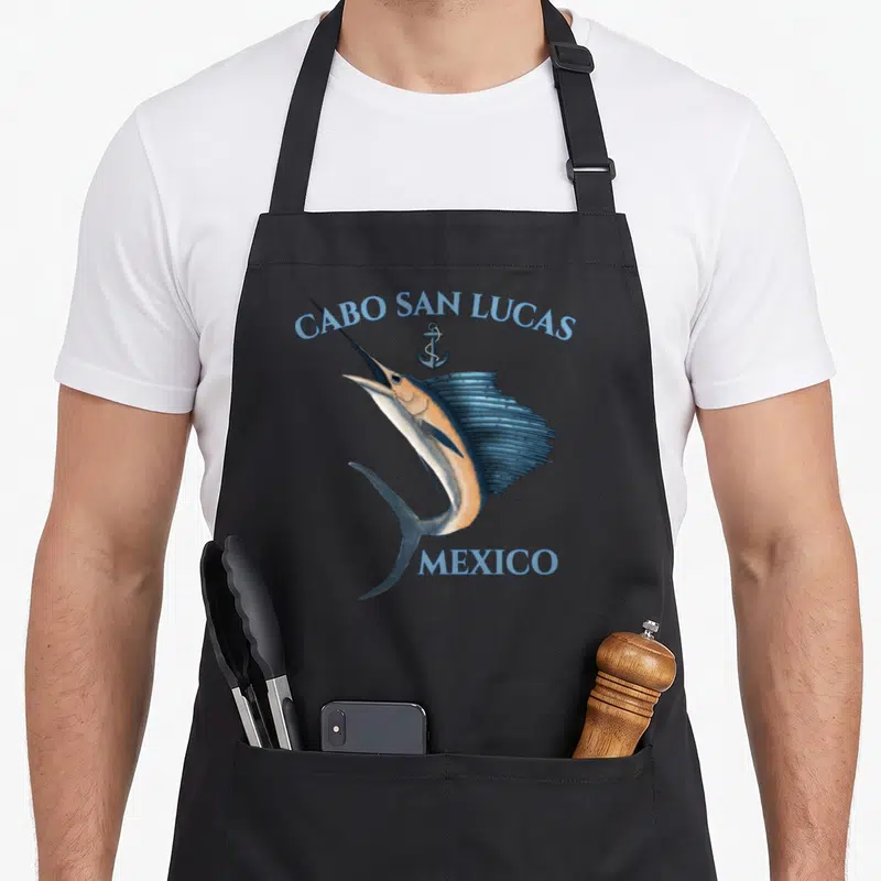 Swordfish mexico apron - Realistic blue marlin jumping below arched CABO SAN LUCAS MEXICO text and small anchor — shown on a black cotton canvas apron against a white background