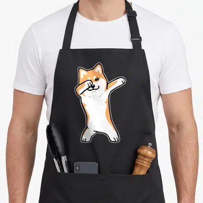 Meme dabbing dog apron - Cartoon Shiba Inu dog in orange and white performing a dab dance pose — shown on a black cotton canvas apron against a white background