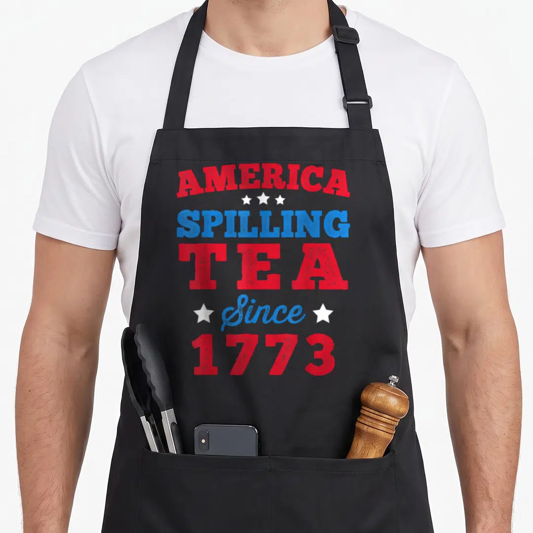 4th tea party aprons - Red and blue stacked text America Spilling Tea Since 1773 with white stars — shown on a black cotton canvas apron against a white background