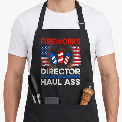 Firework director run 4th of july apron - Red white blue fireworks rockets and distressed flag with sarcastic director — shown on a black cotton canvas apron against a white background