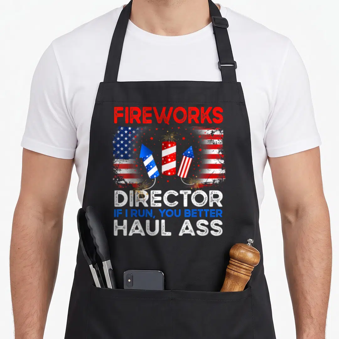 Firework director run 4th of july apron - Red white blue fireworks rockets and distressed flag with sarcastic director — shown on a black cotton canvas apron against a white background