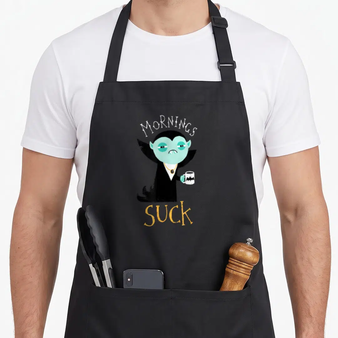 Vampire morning apron - Tired light blue vampire holding bat mug with Mornings Suck text arched above and below — shown on a black cotton canvas apron against a white background