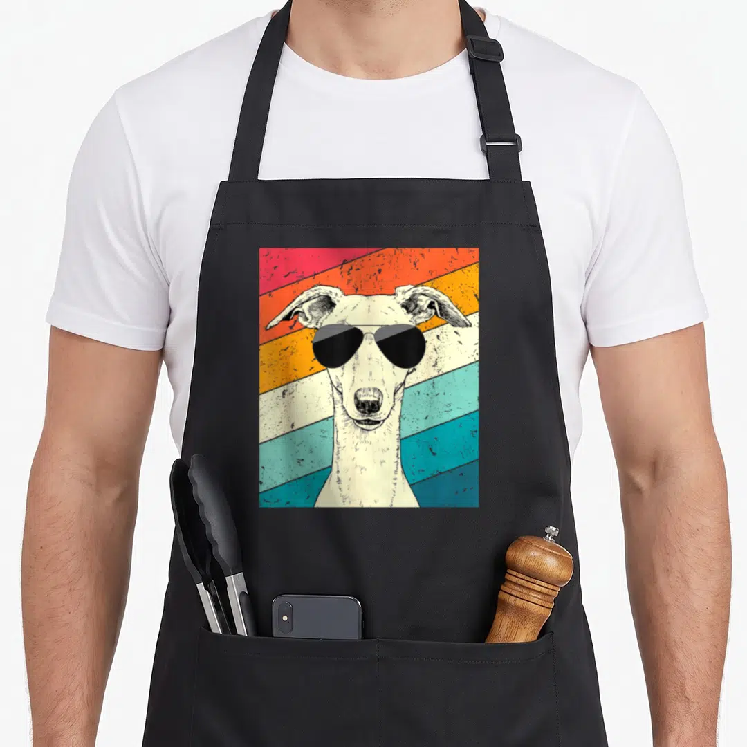 Whippet sunglass dog apron - Retro white whippet with sunglasses against red orange yellow teal and white stripes — shown on a black cotton canvas apron against a white background