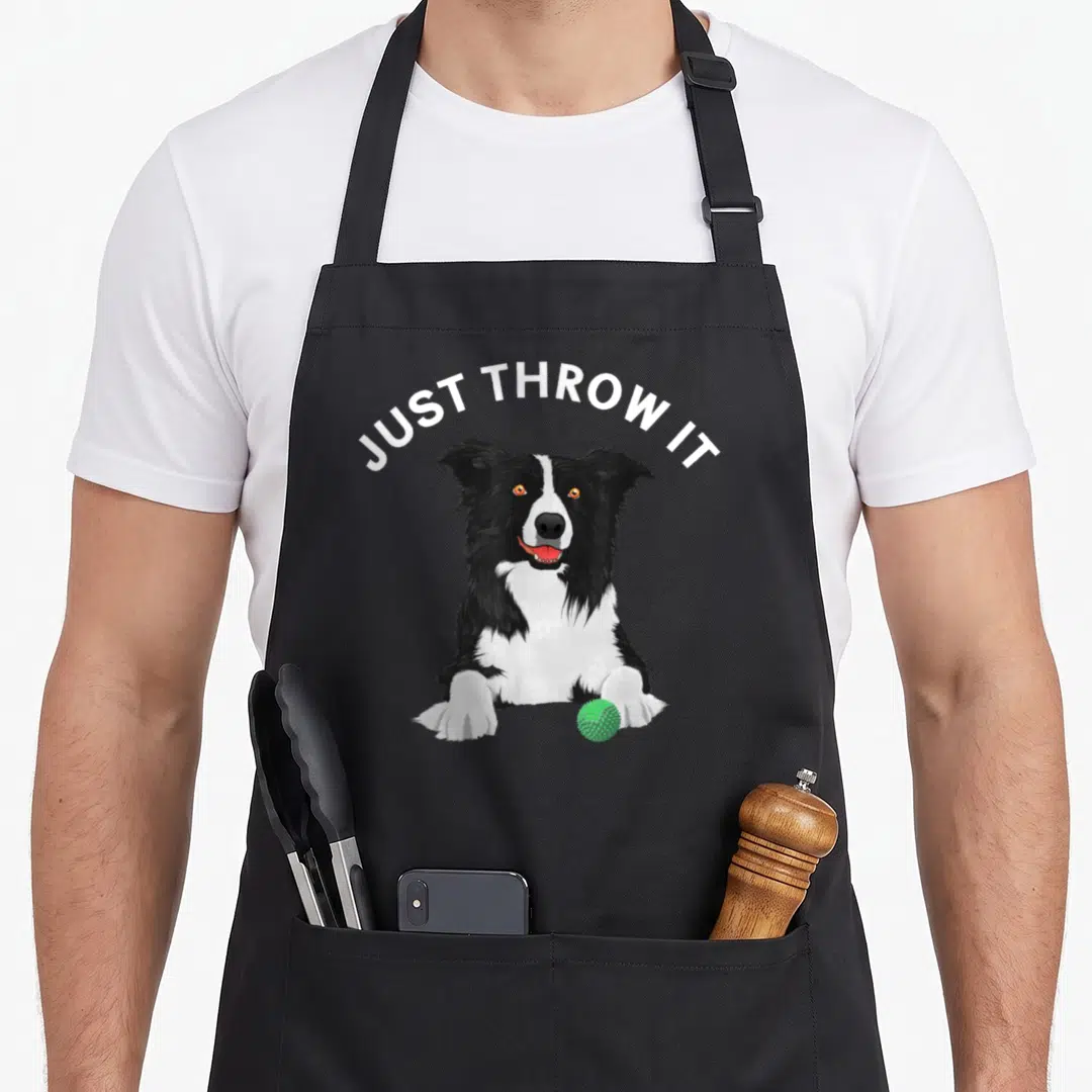 Funny border collie apron - Cartoon black and white dog with green ball and JUST THROW IT text — shown on a black cotton canvas apron against a white background