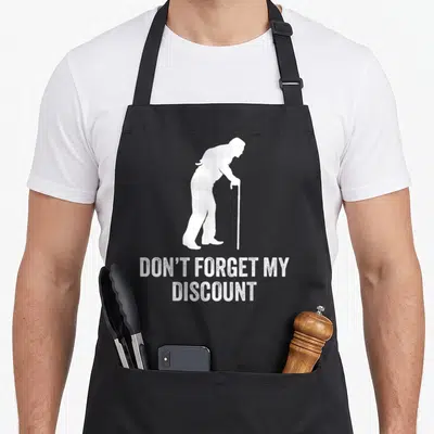 Older birthday gag aprons - White silhouette of elderly man with cane above distressed text reading DON'T FORGET MY — shown on a black cotton canvas apron against a white background