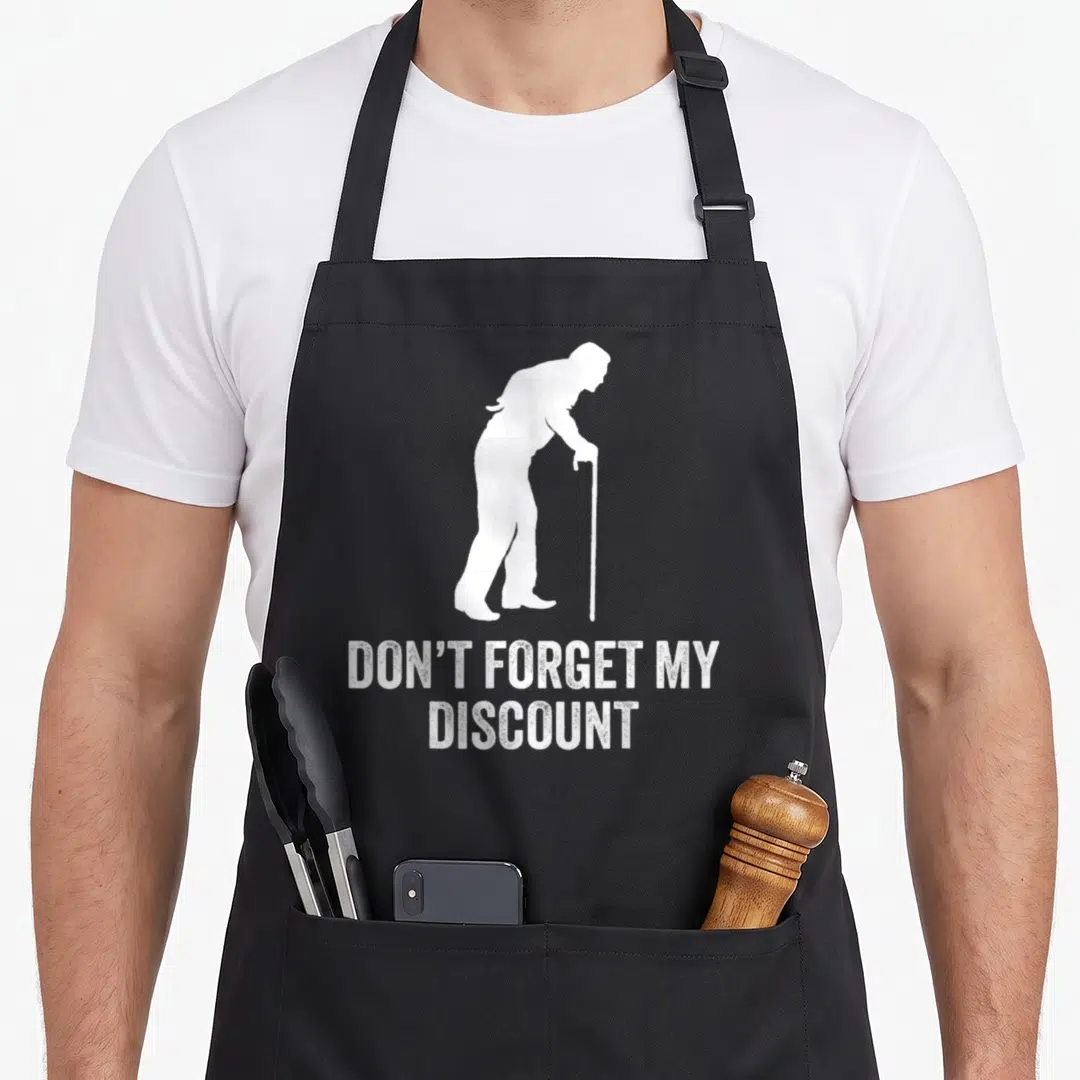 Older birthday gag aprons - White silhouette of elderly man with cane above distressed text reading DON'T FORGET MY — shown on a black cotton canvas apron against a white background