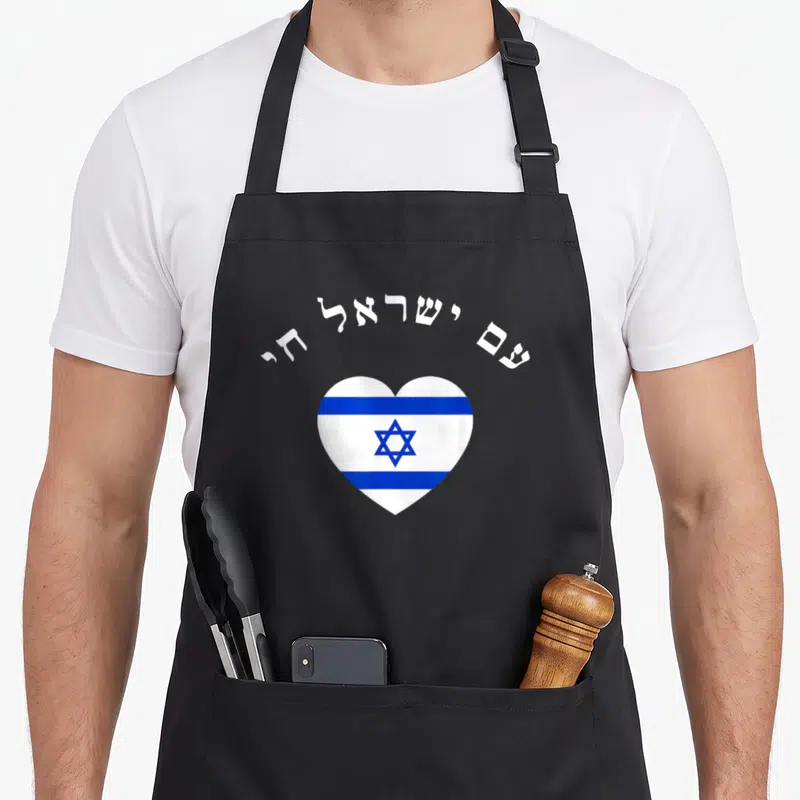 Nation hebrew aprons - White and blue heart shaped flag with arched Hebrew text reading Am Yisrael Chai — shown on a black cotton canvas apron against a white background