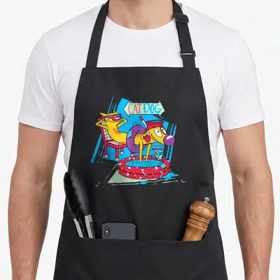 Catdog puddle apron - Yellow cartoon cat-dog lounging on chair and in pool with CAT DOG text in arrow — shown on a black cotton canvas apron against a white background
