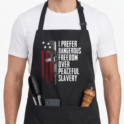 Dangerous pro apron - Rifle graphic with red stripes and stacked text I Prefer Dangerous Freedom Over Peaceful Slavery — shown on a black cotton canvas apron against a white background