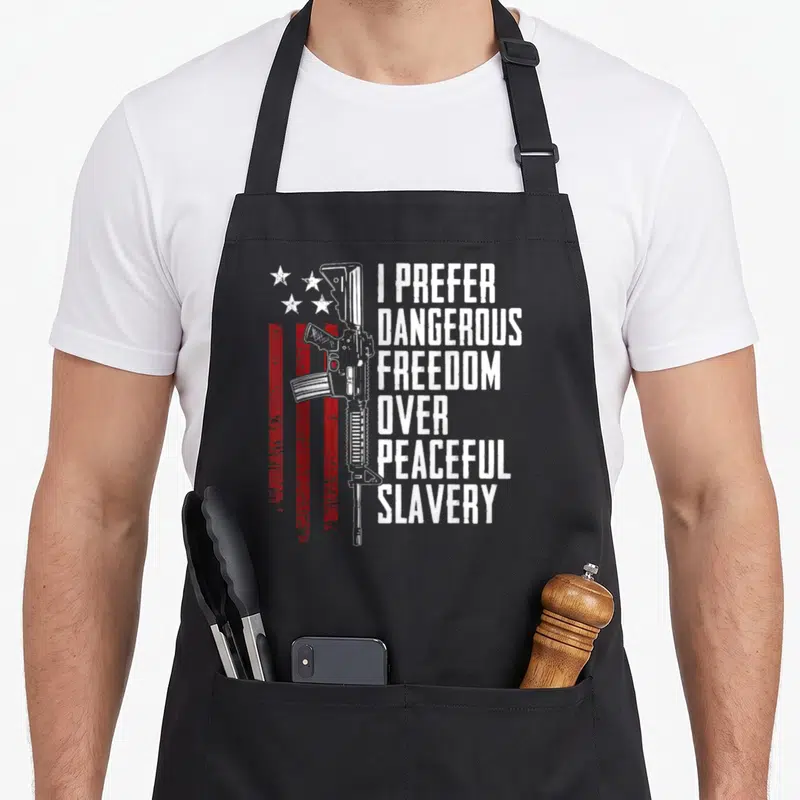 Dangerous pro apron - Rifle graphic with red stripes and stacked text I Prefer Dangerous Freedom Over Peaceful Slavery — shown on a black cotton canvas apron against a white background