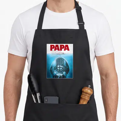 Funny poster ghost apron - PAPA text above swimmer and submerged man in mitre wearing blue water — shown on a black cotton canvas apron against a white background