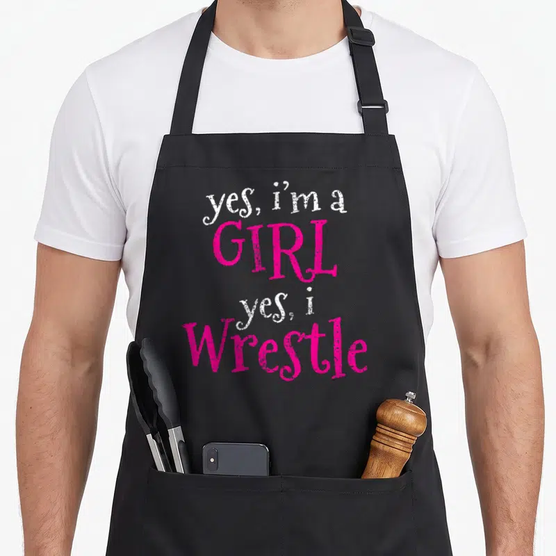 Vintage wrestler wrestling apron - Stacked white and pink text reading yes i'm a girl yes i wrestle — shown on a black cotton canvas apron against a white background