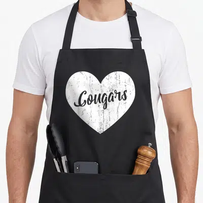 Cougar novelty apron - Distressed white heart with grey Cougars script text on black fabric — shown on a black cotton canvas apron against a white background