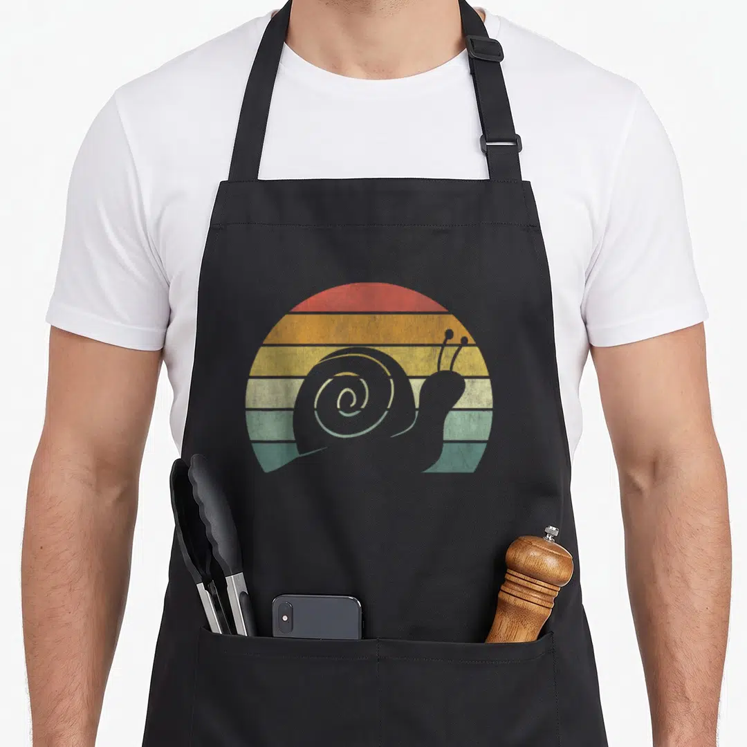 Sunset snail apron - Grey snail silhouette over red orange yellow green teal striped sun — shown on a black cotton canvas apron against a white background