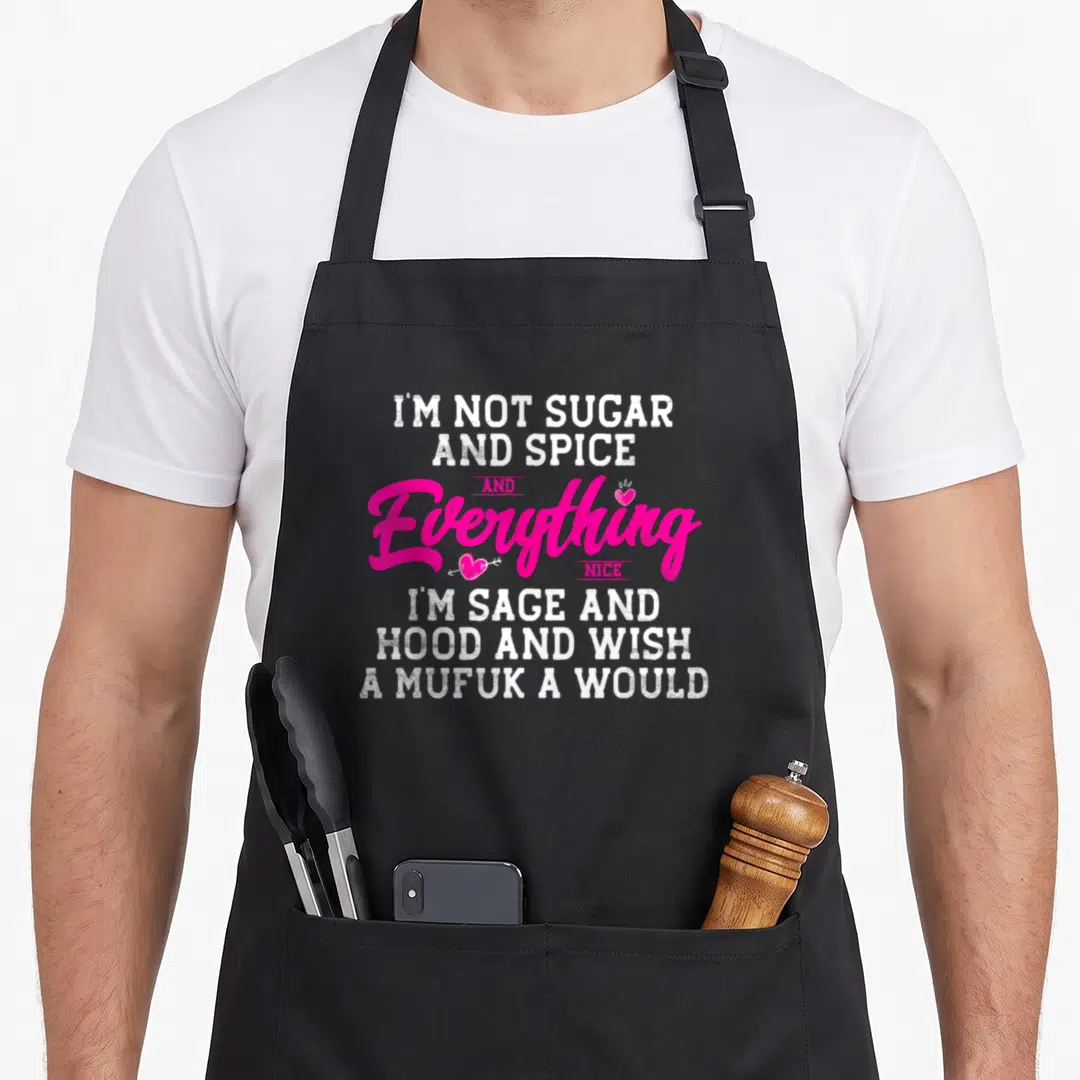Sugar spice sage apron - Stacked white and pink text reading I'm not sugar and spice with two small pink hearts around — shown on a black cotton canvas apron against a white background