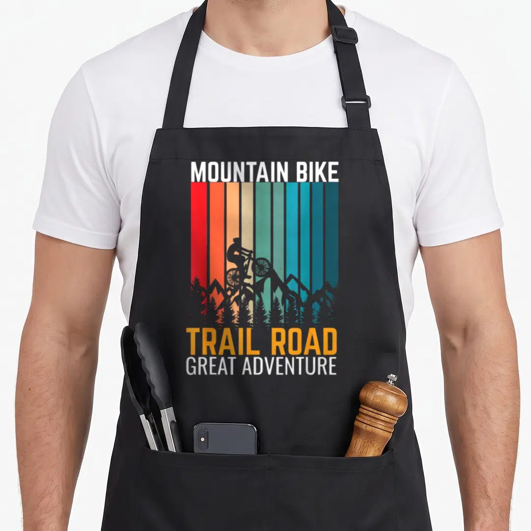 Mountain trail bike apron - Retro biker silhouette over red orange yellow blue white stripes with mountains and trees — shown on a black cotton canvas apron against a white background