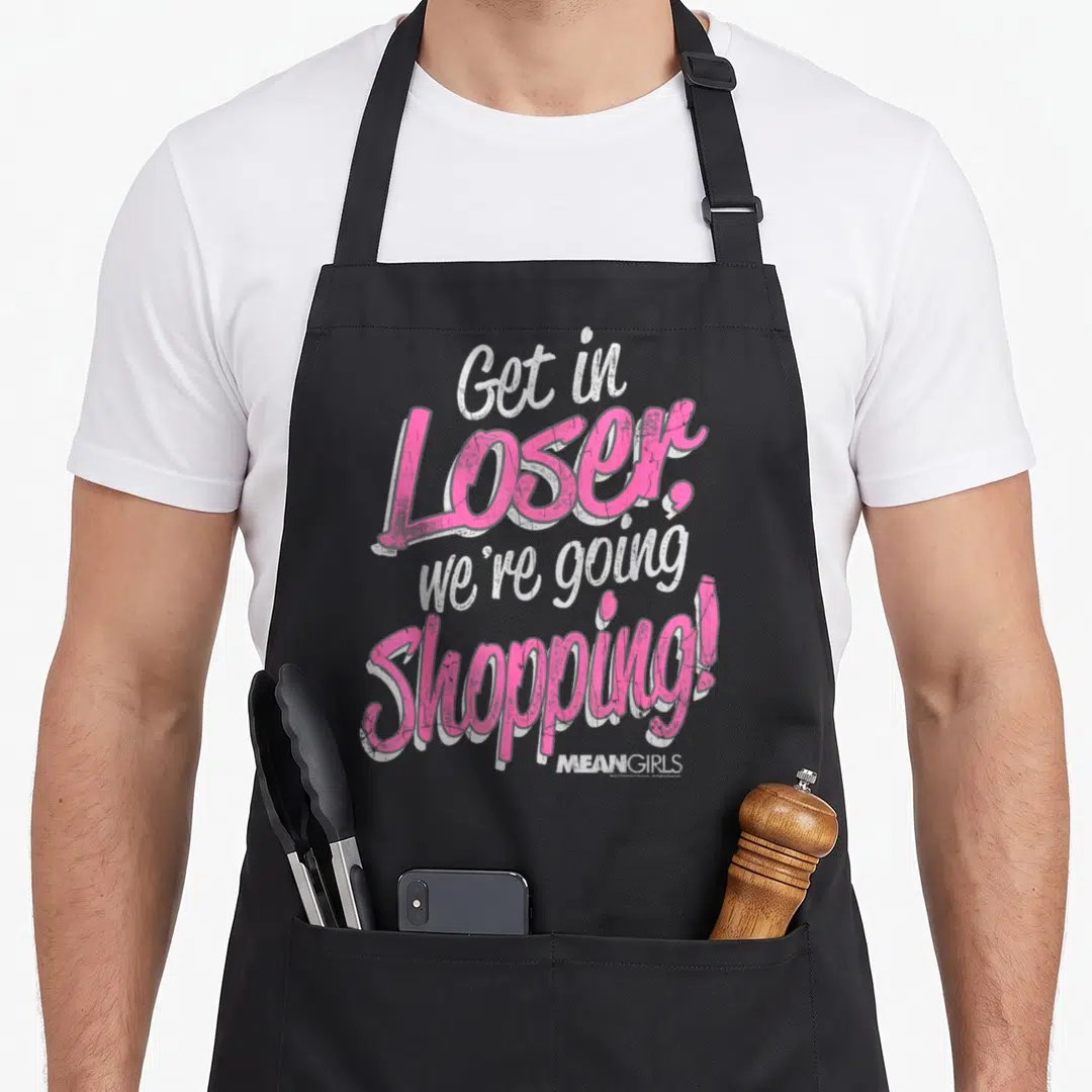 Loser mean girls apron - Pink and white distressed typography reading Get in Loser we're going Shopping — shown on a black cotton canvas apron against a white background