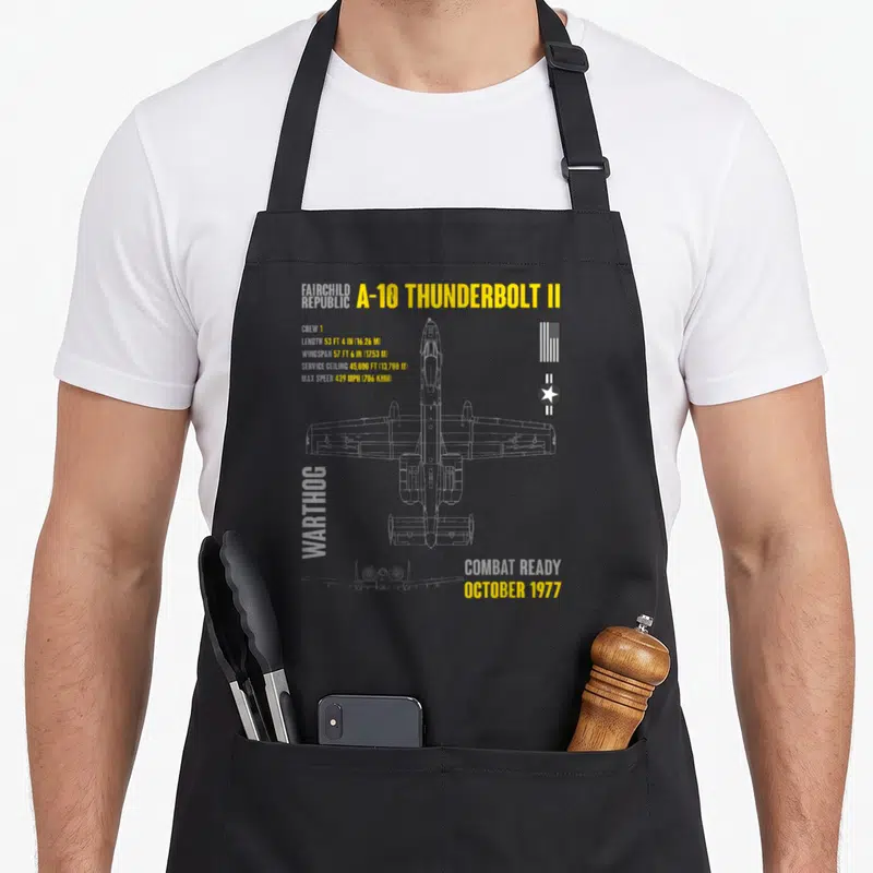 Thunderbolt aircraft apron - A-10 Thunderbolt II top-down line drawing with yellow specs, Warthog text, and US flag — shown on a black cotton canvas apron against a white background