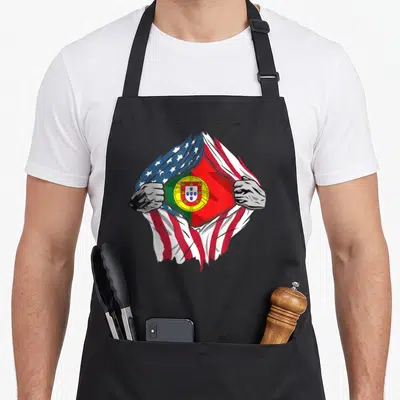 Flag root portuguese apron - Cartoon hands tear USA flag to reveal Portuguese flag with red white blue green yellow — shown on a black cotton canvas apron against a white background