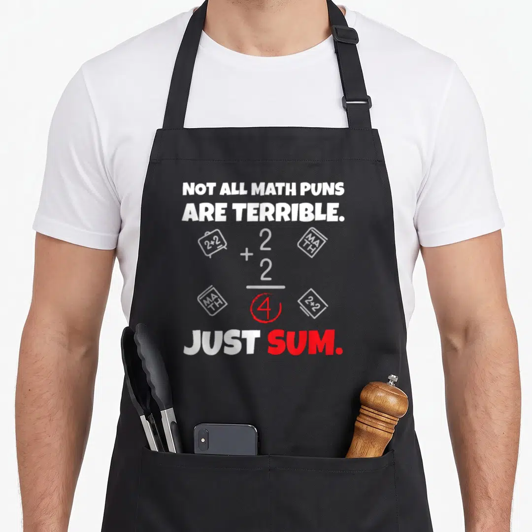 Terrible teacher apron - Not All Math Puns Are Terrible Just Sum text with 2+2=4 equation and book icons — shown on a black cotton canvas apron against a white background