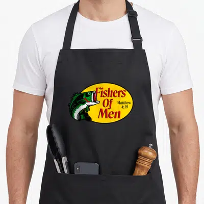 Fisher fishing aprons - Green cartoon fish overlapping yellow oval with red Fishers Of Men text — shown on a black cotton canvas apron against a white background