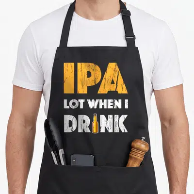 Lot drink beer apron - Distressed orange IPA text above white LOT WHEN I DRINK with brown bottle replacing letter I — shown on a black cotton canvas apron against a white background
