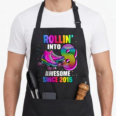 Skating 8th birthday apron - Rainbow roller skates and number 8 with confetti and text Rollin into Awesome Since 2015 — shown on a black cotton canvas apron against a white background
