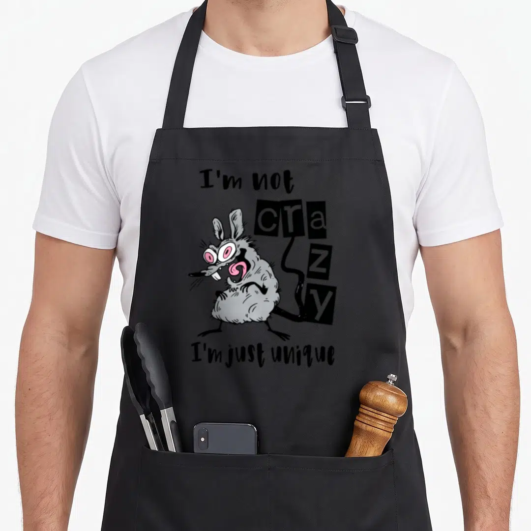 Mouse unique apron - Cartoon grey rat with pink eyes and text I'm not crazy I'm just unique — shown on a black cotton canvas apron against a white background