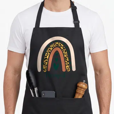 Therapist leopard apron - Minimalist rainbow with four arcs, three hearts, and therapist text in muted colors — shown on a black cotton canvas apron against a white background