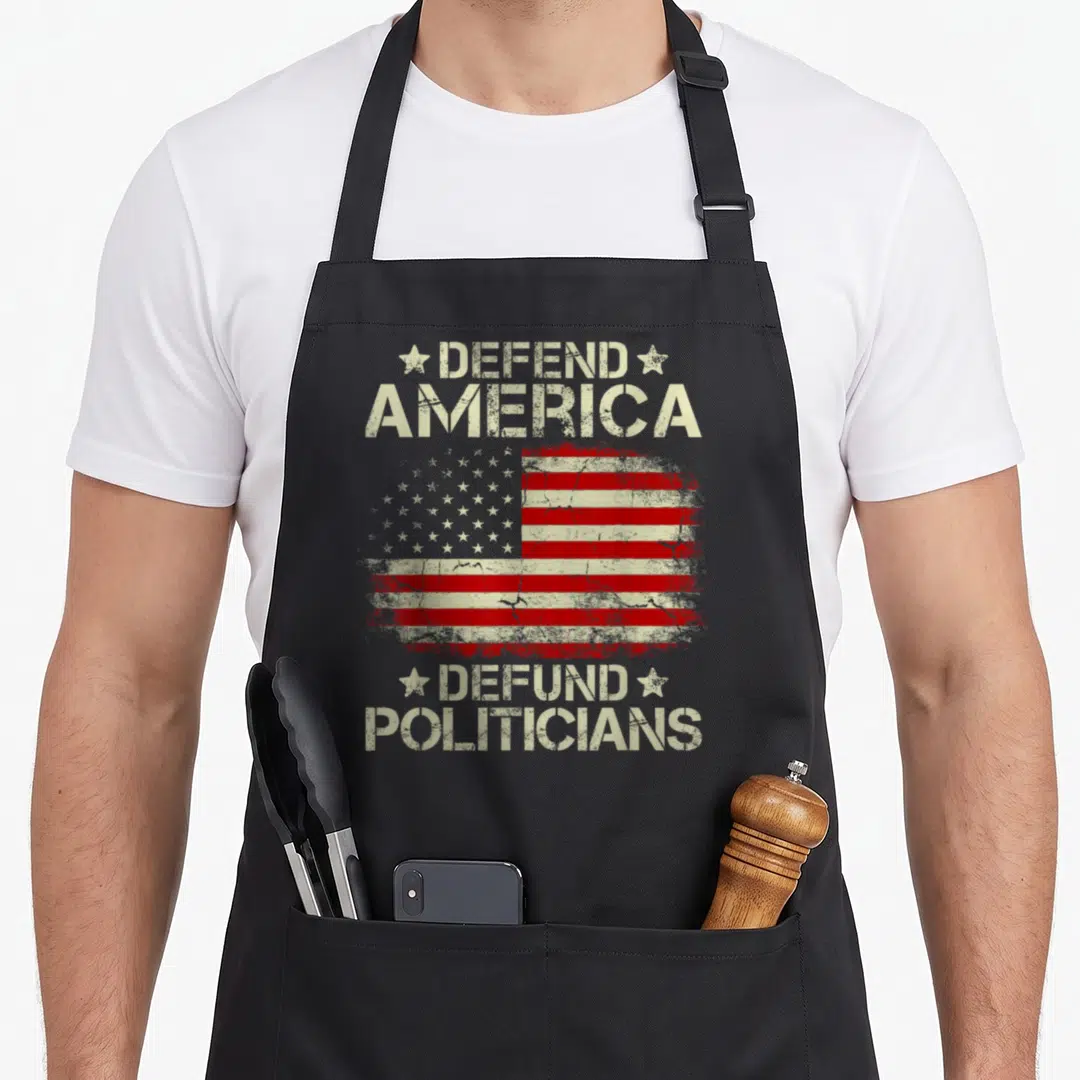 Flag politician apron - Distressed USA flag between Defend America and Defund Politicians stencil text — shown on a black cotton canvas apron against a white background