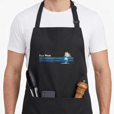 Key tree apron - Key West text white palm tree blue sun distressed stripes — shown on a black cotton canvas apron against a white background