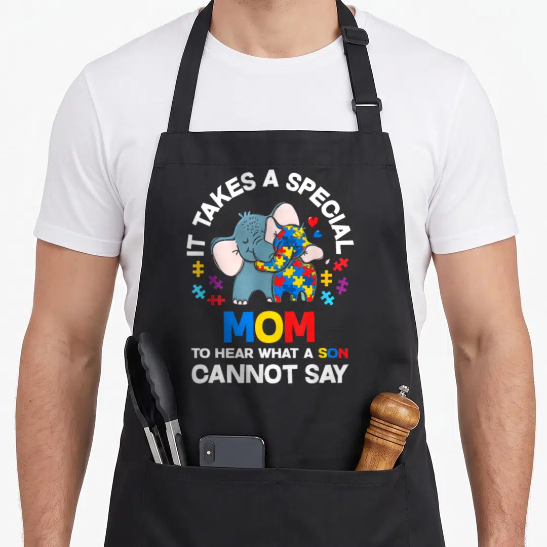 Autism mom and son aprons - Two hugging elephants with puzzle pieces and text about special mom hearing what son cannot — shown on a black cotton canvas apron against a white background