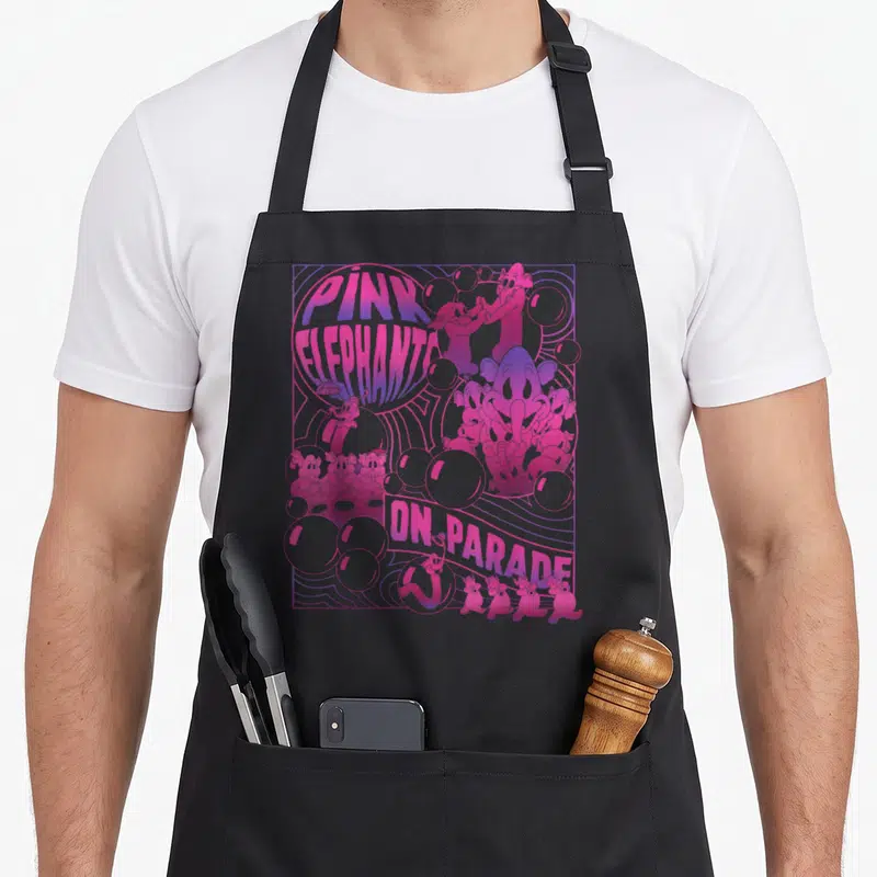Parade elephant print apron - Pink elephants on parade text with cartoon characters, bubbles, and wavy lines in pink — shown on a black cotton canvas apron against a white background