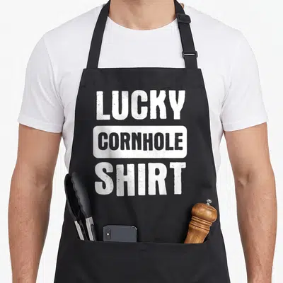 Lucky cornhole bags and aprons - Stacked white and grey text reading LUCKY CORNHOLE SHIRT — shown on a black cotton canvas apron against a white background