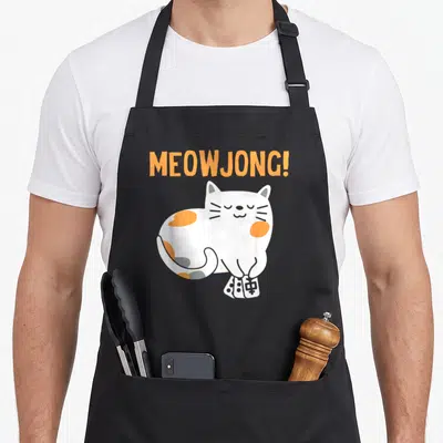 Cat mahjong apron - Orange MEOWJONG text above white and orange cat holding mahjong tiles — shown on a black cotton canvas apron against a white background