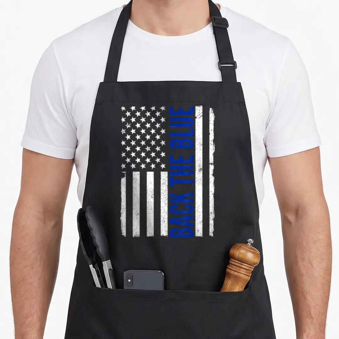 Blue pro apron - Vertical Back The Blue text on distressed white and blue flag with stars — shown on a black cotton canvas apron against a white background