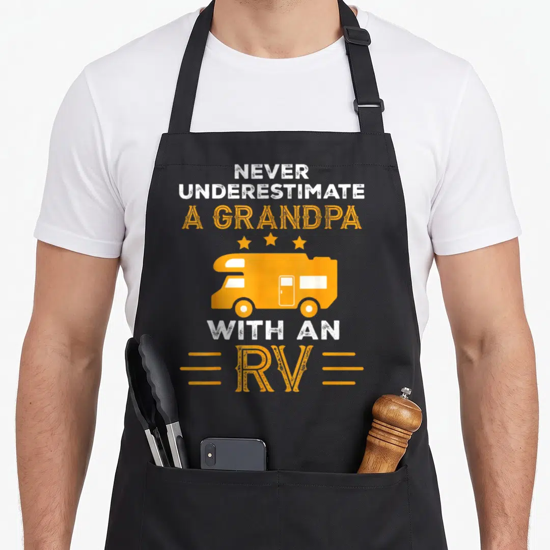 Underestimate grandpa apron - Orange RV illustration with white and orange text reading Never Underestimate A Grandpa — shown on a black cotton canvas apron against a white background