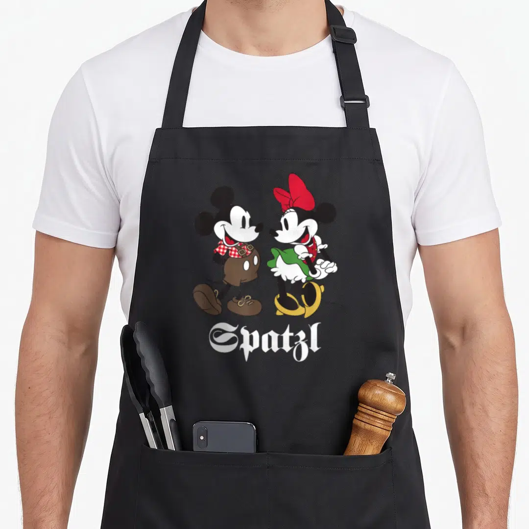Mouse oktoberfest apron - Mickey and Minnie Mouse in Bavarian clothes with Spatzl text below in cartoon style — shown on a black cotton canvas apron against a white background