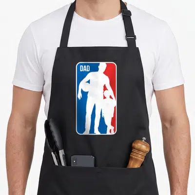 Basketball father day apron - White dad and son silhouettes holding a basketball on split blue and red background — shown on a black cotton canvas apron against a white background