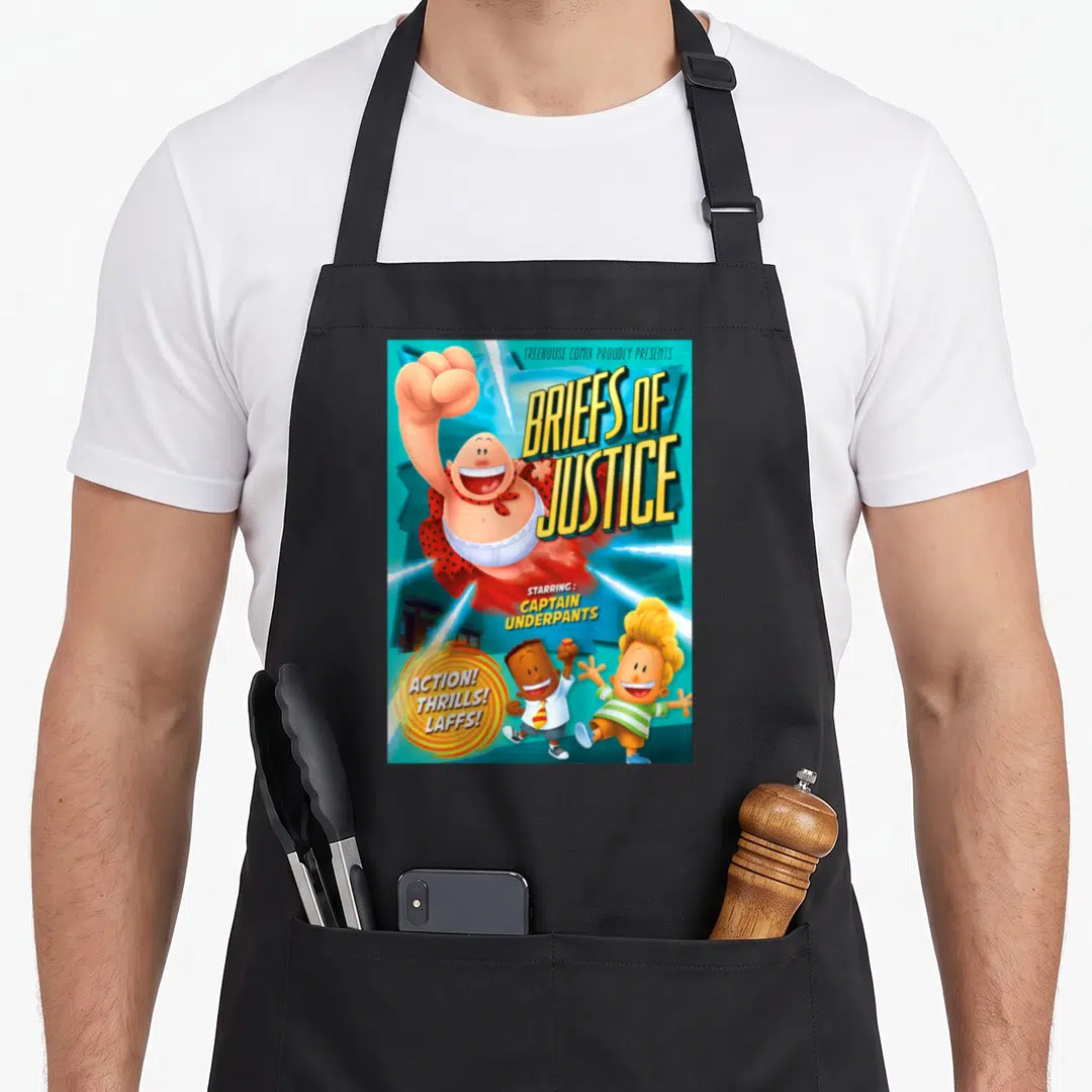 Captain girl birthday apron - Comic cover art of Captain Underpants flying with two boys and bold yellow text on blue — shown on a black cotton canvas apron against a white background