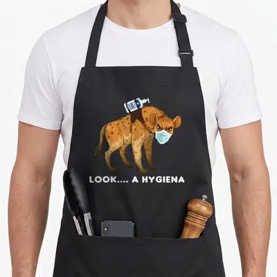 Hyena face apron - Cartoon hyena in blue mask carrying sanitizer bottle with text LOOK A HYGIENA — shown on a black cotton canvas apron against a white background